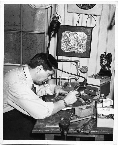 David Smith working on a bronze plaque, with Widow's Lament, 1942 (unfinished state), Munitions Makers, 1939, Detail of Bombing Civilian Populations, 1939, and Head, 1938, and drawing in frost on window, in Schenectady, New York, 1940. Gelatin silver print. 10 x 8 in. (25.4 x 20.3 cm) (c) Estate of David Smith/VAGA, NY.