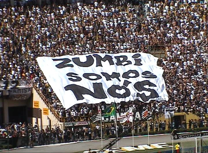 la imagen muestra una multitud en las gradas de un estadio de fútbol sujetando una pancarta muy grande que ocupa varias filas de la grada con la inscripción «Zumbi somos Nós»