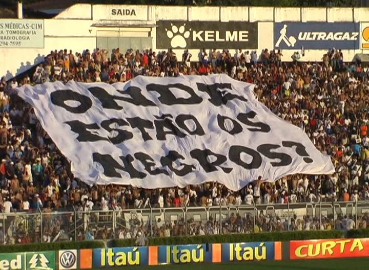 La imagen muestra una multitud en las gradas de un estadio de fútbol sujetando una pancarta muy grande que ocupa varias filas de la grada con la inscripción «Zumbi somos Nós»