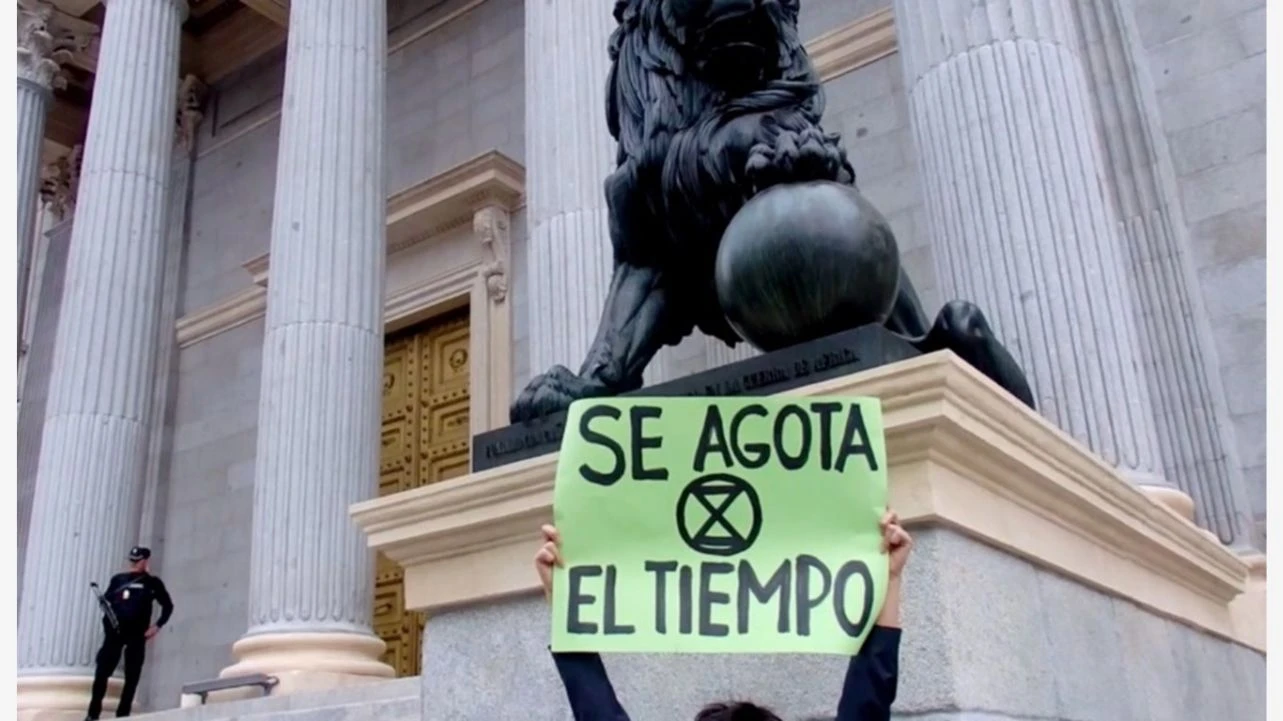 Activista anónima sostiene un cartel del movimiento Extinction Rebellion con la frase “Se agota el tiempo” ante la Puerta de los leones del Congreso de los Diputados en Madrid, 2024. MoPiGra, Creative Commons Attribution 4.0