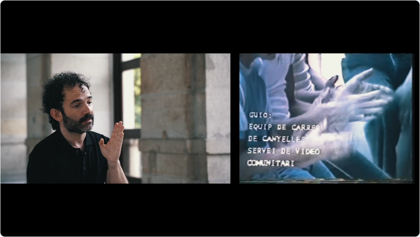Un hombre con el pelo rizado negro y una camisa negra habla sentado en el claustro del Museo, a la derecha se ve una imagen de un vídeo vhs con unas manos que palmean. Sobre la imagen, unos créditos.