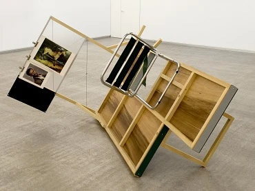 Txomin Badiola. Le radeau (¿qué es lo que veo?¿qué es lo que no ves?), 2015. Construcción en madera parcialmente pintada, acero galvanizado y pintado, plexiglás con marco de aluminio, materiales impresos, silla tubular. Colección del artista, Bilbao