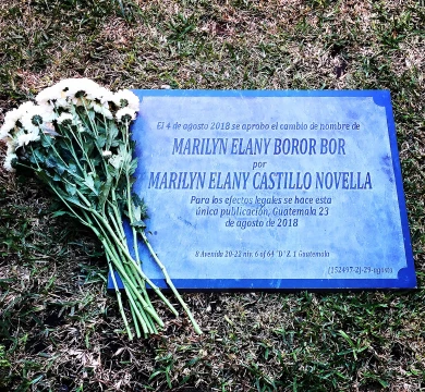 Fotografía de un ramo de flores junto a una lápida con inscripción que informa del cambio de nombre de Marilyn Elany Boror Bor a Marilyn Elany Castillo Novella, fechada en Guatemala el 23 de agosto de 2018.