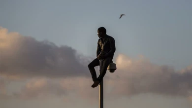 Un migrante subsahariano se sienta sobre un poste en una valla metálica que divide Marruecos y el enclave español de Melilla. Santi Palacios, Melilla, 2014